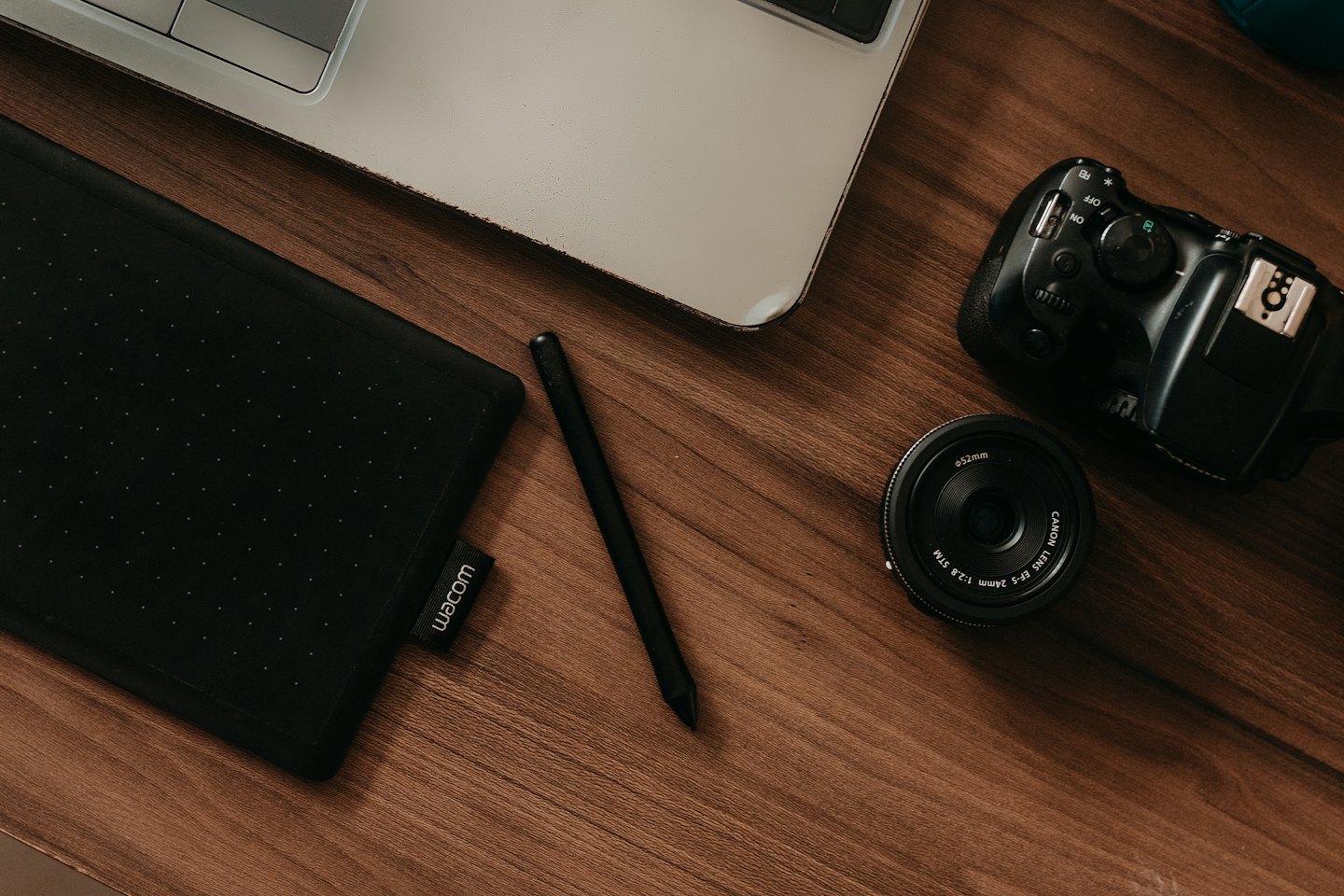 Ahşap masada dizüstü bilgisayar, grafik tablet, kalem ve kamera ekipmanları.